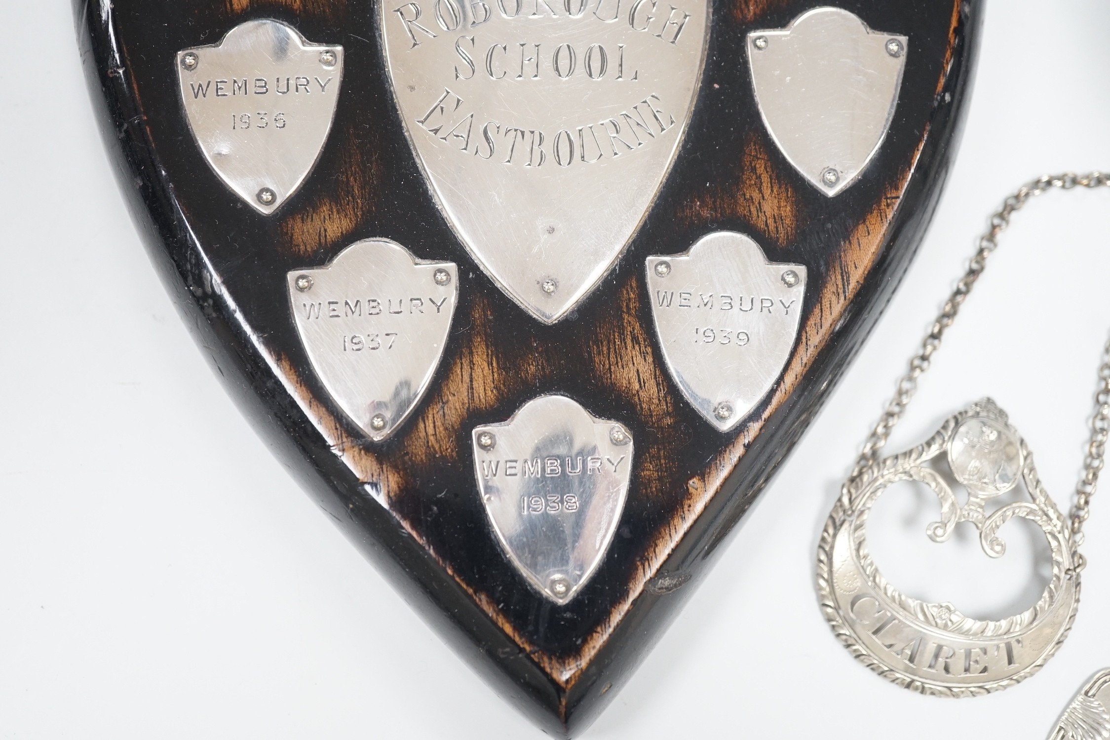 A small 1930's silver christening mug, two 19th century silver decanters labels 'Claret' and 'Marsala' and a white metal mounted polished wood shield 'Roborough School, Eastbourne Chess' and a Victorian silver oval musta